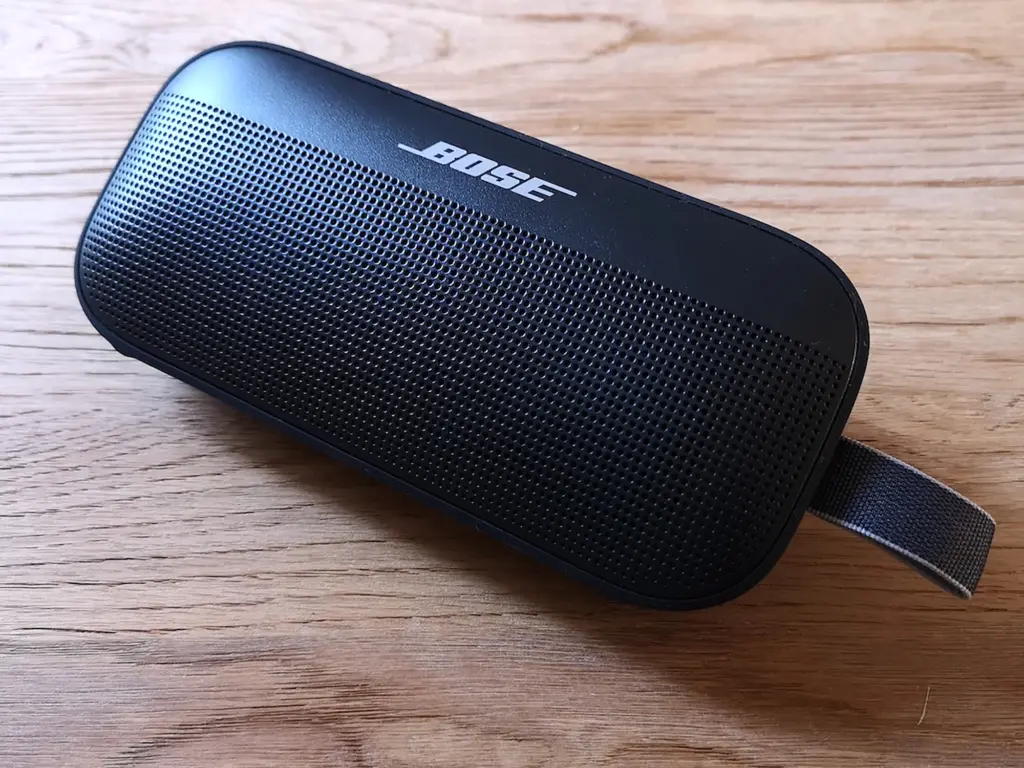 Compact black Bose portable speaker with perforated front grille and fabric loop on wooden surface