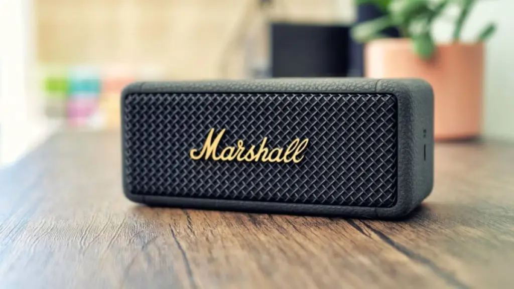 Compact black Marshall portable speaker with textured front grille and gold logo on a wooden surface