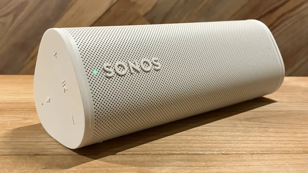 White cylindrical portable speaker with perforated grille, Sonos logo, and control buttons on one end, placed on a wooden surface