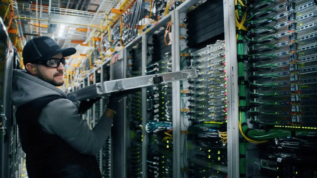 Technician wearing safety glasses and gloves installs or removes a server unit in a data center filled with cables and blinking lights