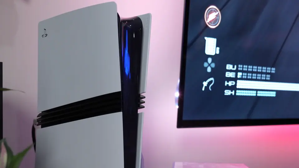Close-up of a white and black gaming console next to a screen displaying game stats on a pink-lit background